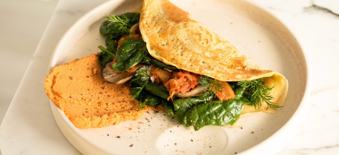 Herb and vegetable omelette with spinach, tomatoes, and dill, served with hummus on a white plate.